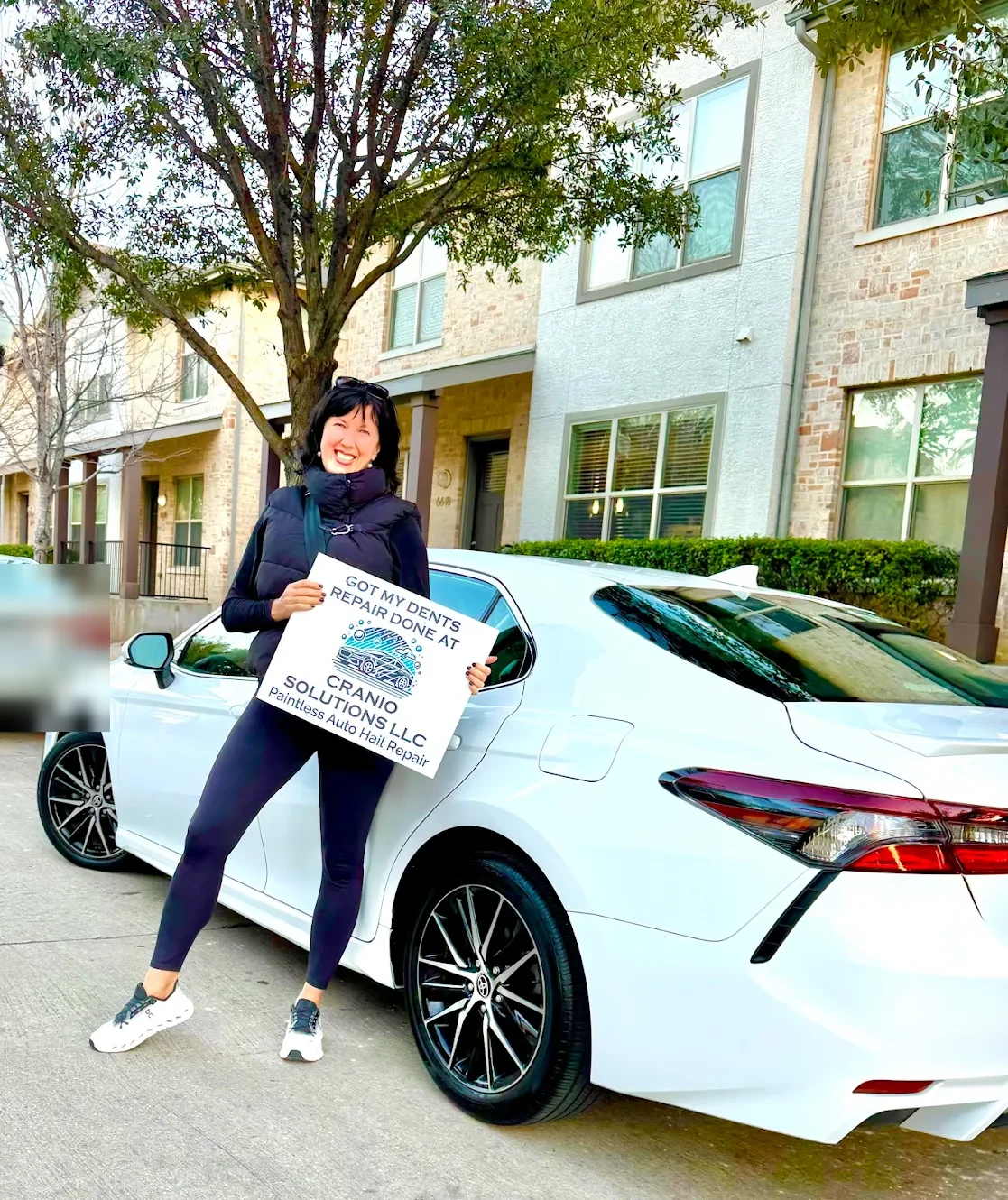 Customer holding a Cranio Hail sign beside her repaired Toyota Camry