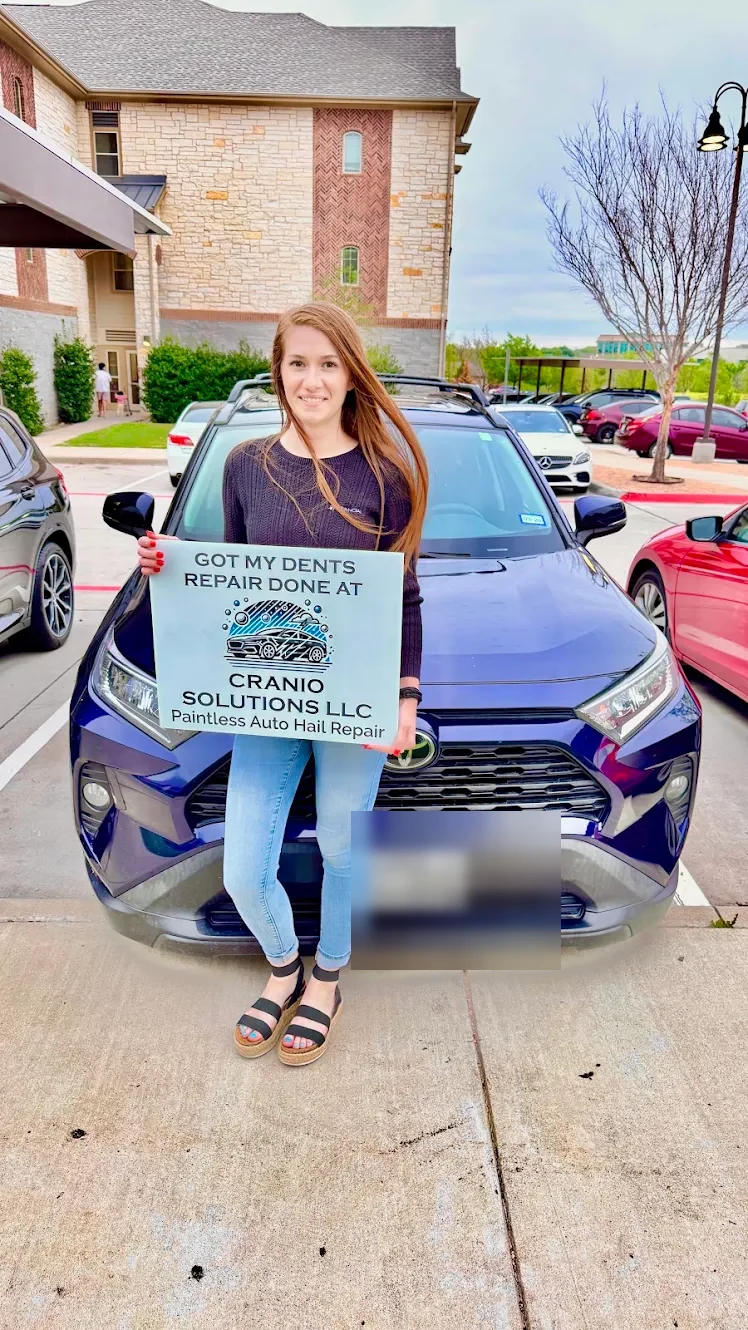 Customer holding a Cranio Hail sign in front of her repaired Toyota